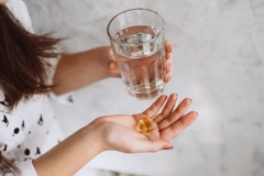 Diet. Nutrition. Girl's hands with pills with cod liver omega-3 oil and a glass of fresh water. The concept of a healthy diet and lifestyle. Vitamin D, E, fish oil capsules.