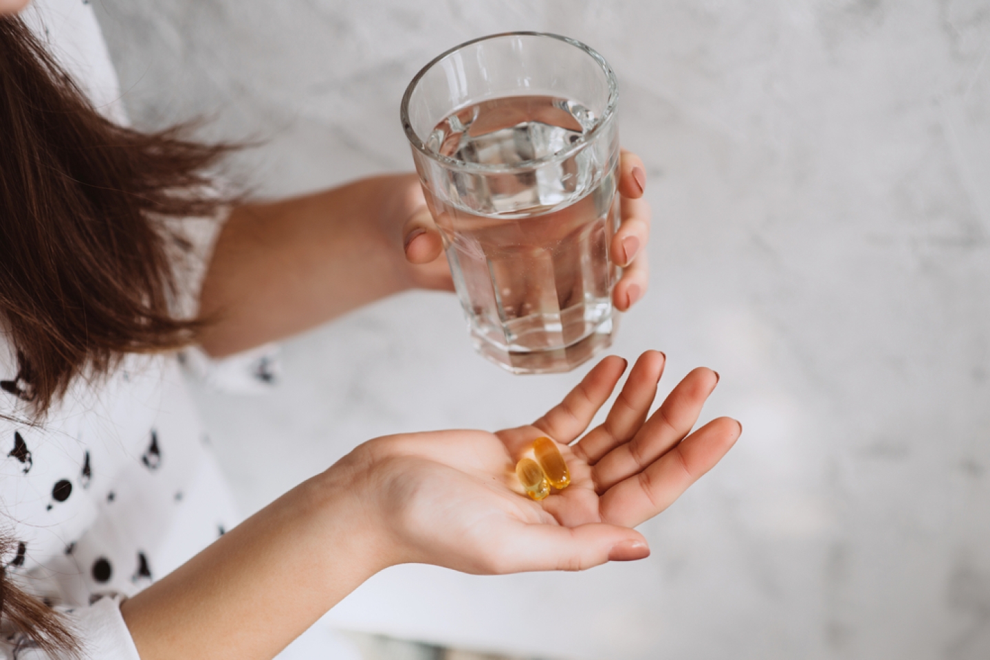 Diet. Nutrition. Girl's hands with pills with cod liver omega-3 oil and a glass of fresh water. The concept of a healthy diet and lifestyle. Vitamin D, E, fish oil capsules.