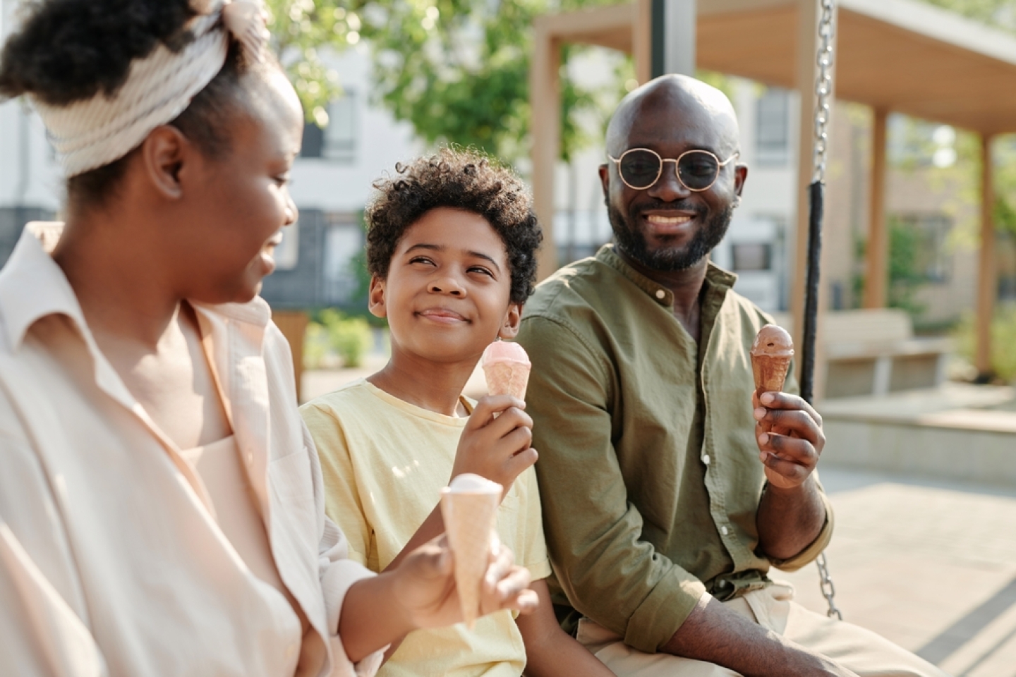 Happy African American family eating ice cream together outdoors while sitting on the swing