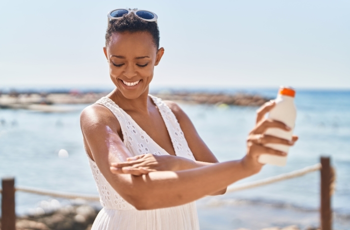 African american woman smiling confident applying sunscreen lotion at seaside